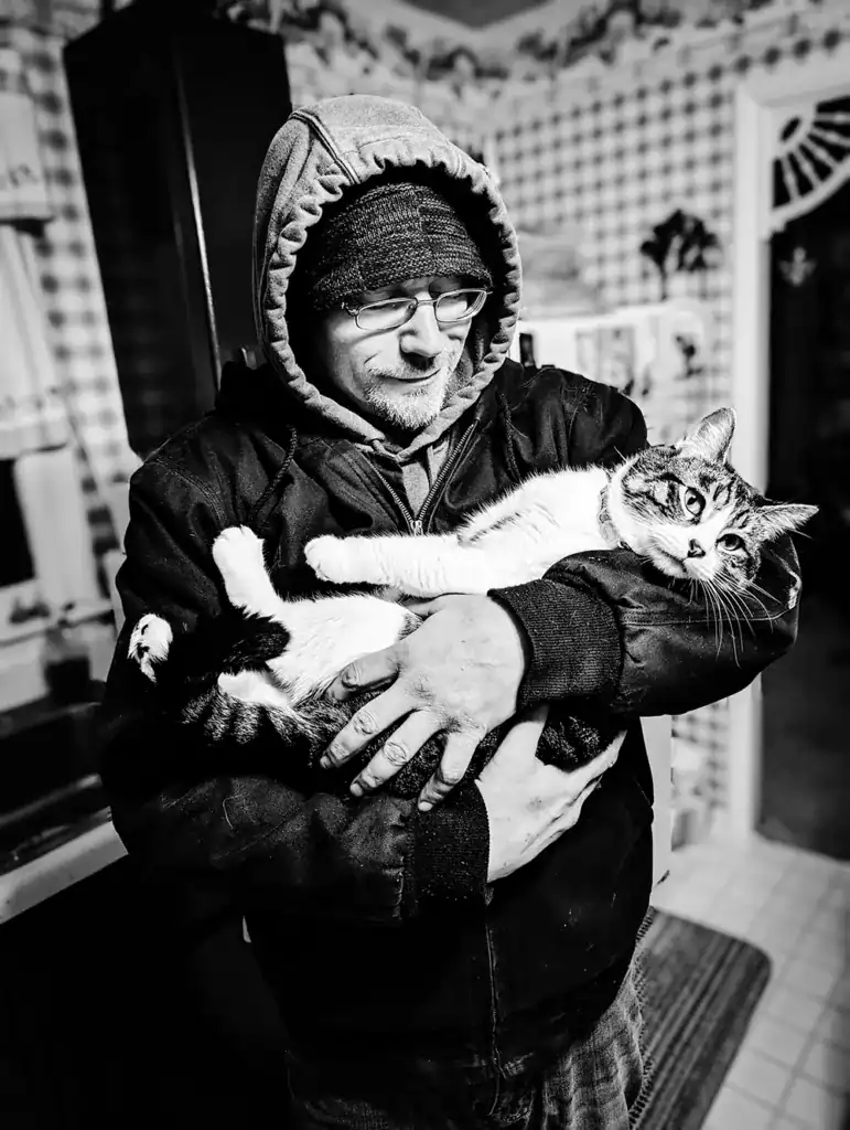 Mature man holding a tabby cat in cozy indoor setting, black and white photo.