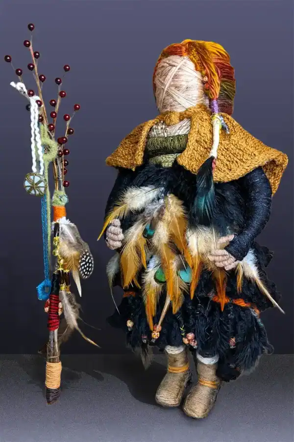 Ella the forest spirit art doll is adorned with feathers and gemstones, holding a walking stick with essential oil diffusers.