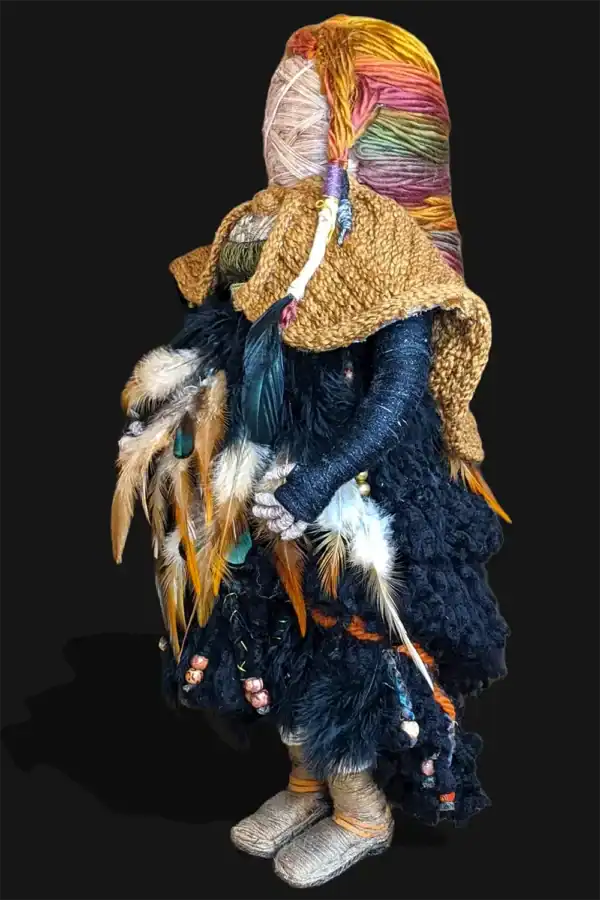 Side view of Ella the forest spirit art doll, highlighting her intricate cloak, feathered dress, and colorful braided hair. She stands without her walking stick.