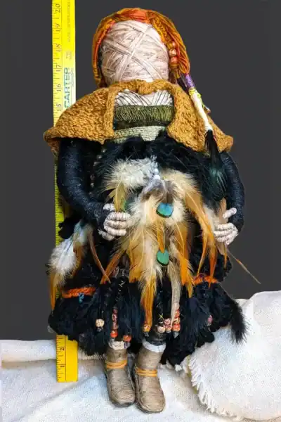 Ella the forest spirit art doll standing in front of a yardstick, showing her height of 20 inches. She is adorned with feathers, beads, and a handmade cloak.
