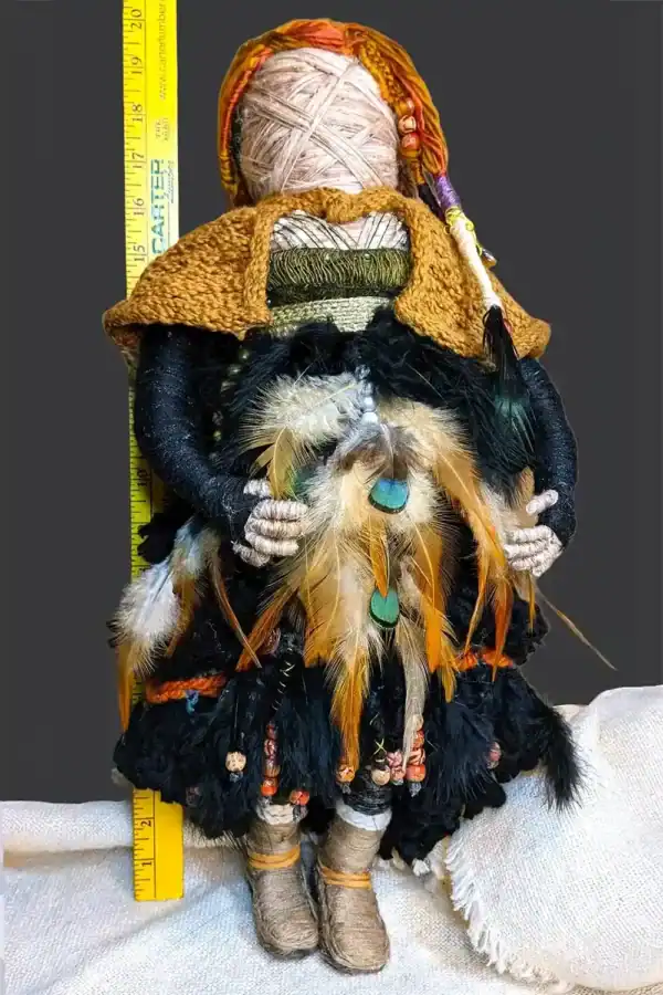 Ella the forest spirit art doll standing in front of a yardstick, showing her height of 20 inches. She is adorned with feathers, beads, and a handmade cloak.