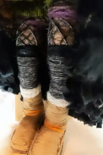Close-up of Ella the forest spirit art doll's legs, showing her boots, leg warmers, fishnet stockings, and green and purple bloomers beneath her skirt.