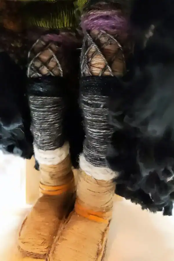 Close-up of Ella the forest spirit art doll's legs, showing her boots, leg warmers, fishnet stockings, and green and purple bloomers beneath her skirt.