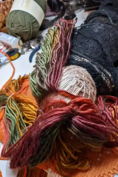 Ella the forest spirit art doll having her multicolored yarn hair added strand-by-strand, with her body wrapped in netting to protect her clothes in progress.
