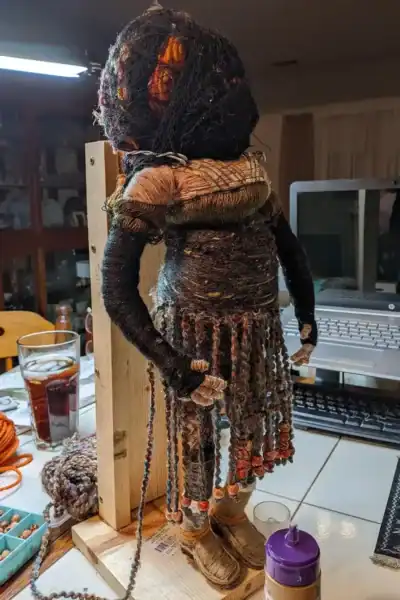 Ella the forest spirit art doll with her head wrapped in netting, showing her boots, off-the-shoulder dress, and asymmetrical under-skirt in progress.