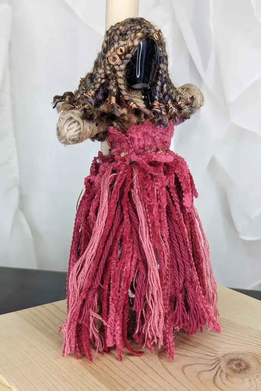 3/4 right-side view of Absynthe Healing Art Doll showcasing her Blue Tiger’s Eye gemstone head, braided multicolored yarn hair with copper accents, and a vibrant pink dress, displayed in a natural background setting.