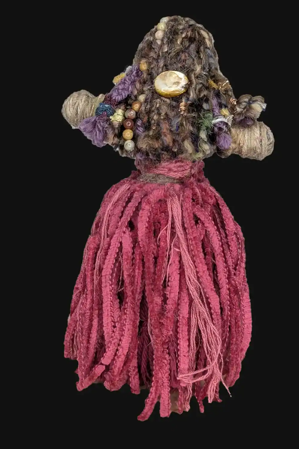 Back view of Absynthe Healing Art Doll showcasing her intricate hairstyle of multicolored yarn, adorned with a shell barrette and copper coils, paired with a vibrant pink skirt, set against a black background.