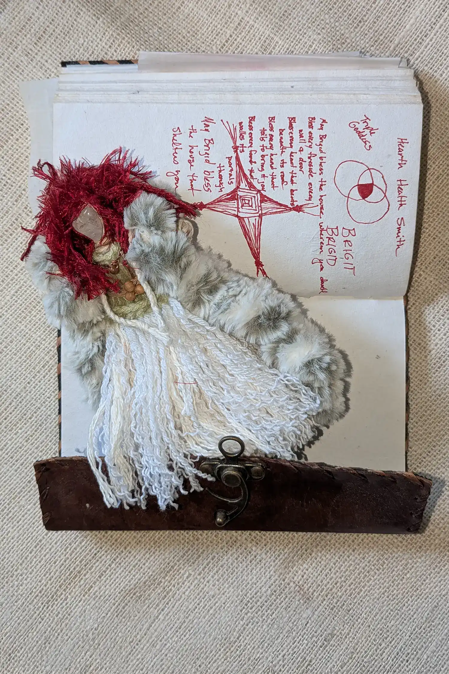 Brigit lying on a journal page with her symbols and handwritten blessing visible.