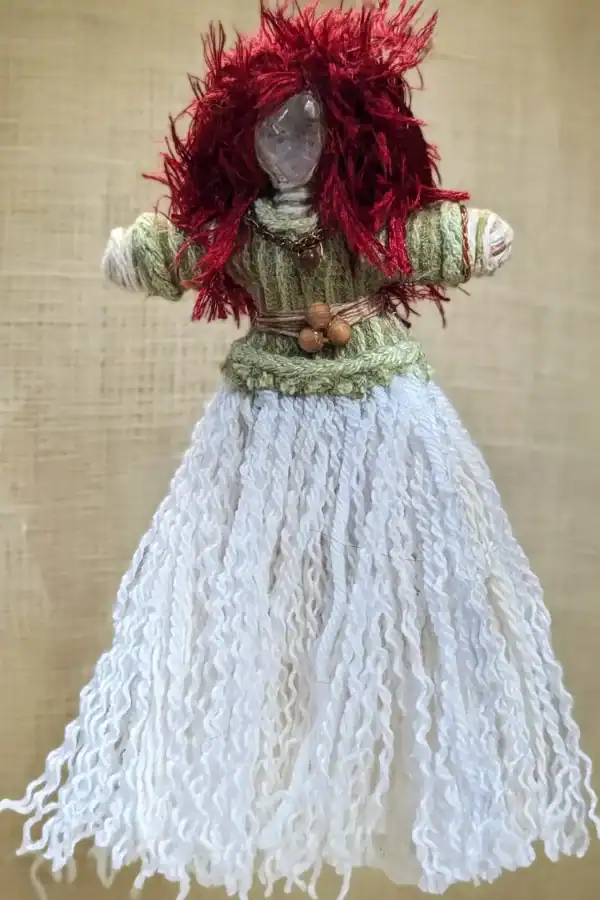 You-Do-You Voodoo™ art doll of Brigit shown in full without her coat, featuring a quartz crystal head, bright red yarn hair, a sage-green top, and a flowing white skirt. A belt of three wooden beads at her waist symbolizes the triple goddess.
