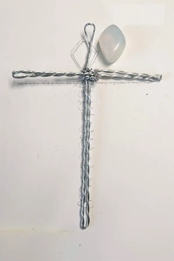 A cross handmade from twisted silver wire, with a smooth pale blue stone resting at the top