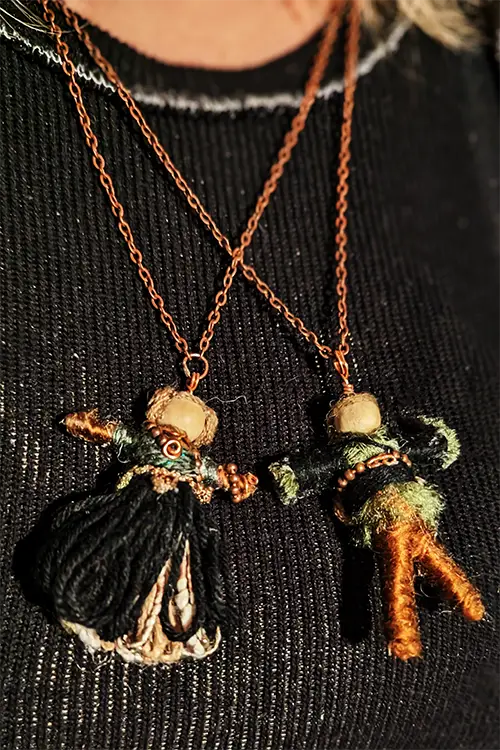 Two two-inch dolls dangling from their chains and wearing green, black, brown and tan.